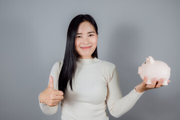 Lovely woman with long dark hair holding piggybank on gray background