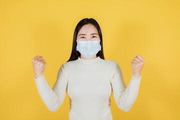 Asian woman in medical face mask to protect Covid-19 (Coronavirus) raise hands glad excited cheerful on yellow background