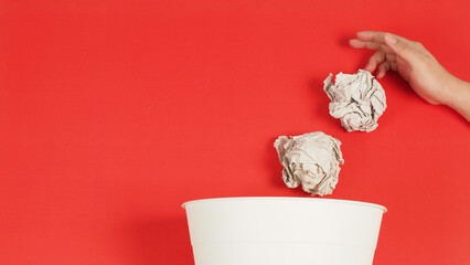 The crumpled white paper is mauled with thand and a trash can on red background.