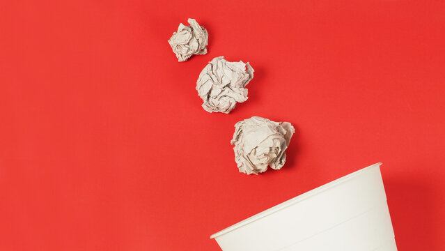 The crumpled white paper is mauled and a trash can on a red background.