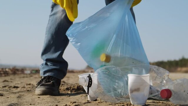 Volunteer wearing gloves cleaning garbage on the beach. Woman collect plastic in a trash bag. Environmental problems, save the planet concept.