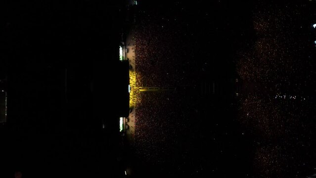 toma cinem&aacute;tica de drone en cenital de Multitud de gente espectadora de un concierto en un festival de m&uacute;sica latina con luces amarillas ilumin&aacute;ndolos 