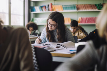 Girl writing while sitting at desk during exam in classroom