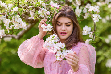 a young woman in a pink dress posing next to a blossoming apple, spring portrait.