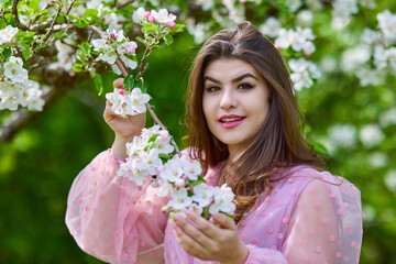 Fototapeta premium a young woman in a pink dress posing next to a blossoming apple, spring portrait.