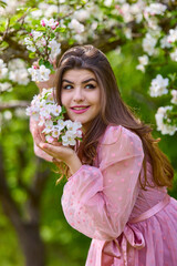 Obraz premium a young woman in a pink dress posing next to a blossoming apple, spring portrait.
