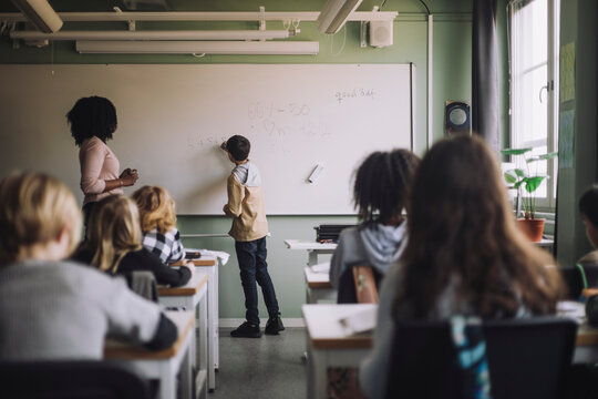 Student solving maths sum on white board in classroom