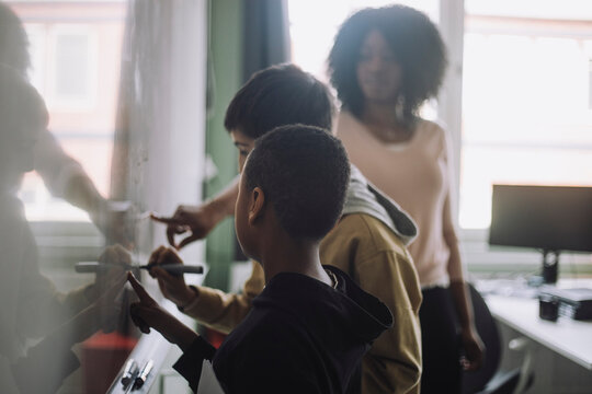 Teacher assisting students while doing mathematics on white board in classroom