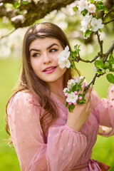 Fototapeta premium a young woman in a pink dress posing next to a blossoming apple, spring portrait.
