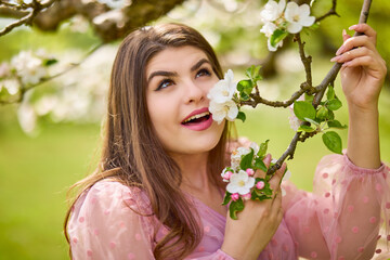 Fototapeta premium a young woman in a pink dress posing next to a blossoming apple, spring portrait.