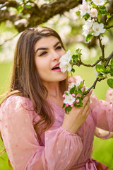 a young woman in a pink dress posing next to a blossoming apple, spring portrait.