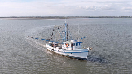 Low aerial view of a shrimp boat pulling nets off the coast of South Carolina, USA. - obrazy, fototapety, plakaty