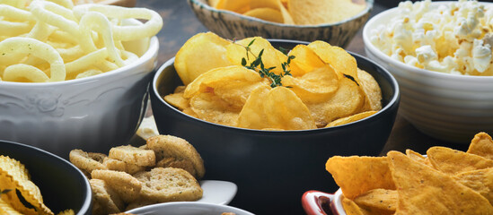 Unhealthy food or snacks. All classic potato snacks with peanuts, popcorn and onion rings and salted pretzels in bowl plates on old wooden background. Unhealthy food for figure, heart, skin, teeth.