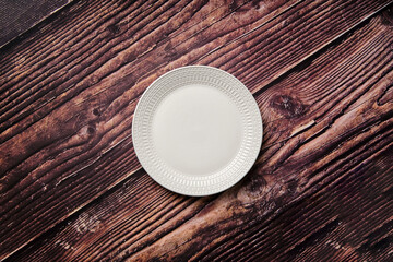 A small white plate with a circular dimple dash pattern against a rustic wooden background is taken from above in the centre.