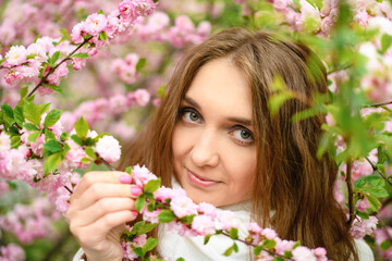 Naklejka premium Beautiful girl and blooming garden, portrait. Girl in white coat with blooming sakura, apple tree