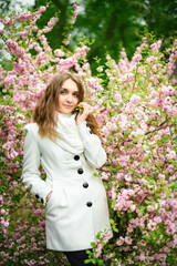 Beautiful girl and blooming garden, portrait. Girl in white coat with blooming sakura, apple tree