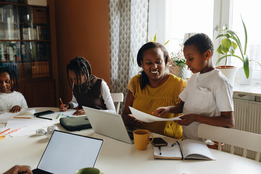 Son showing painting to mother while siblings studying at home
