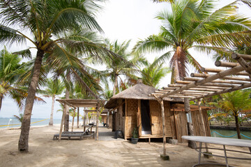 Bungalow and deck chairs on a sandy beach among palm trees by the seashore