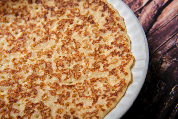 Plain sweet pancake on a small white plate against a wooden background close up.