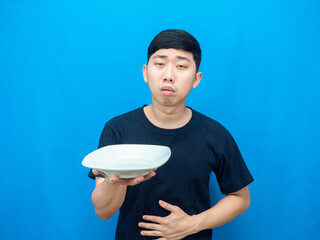 Man holding dish and touch belly feeling hungry blue background