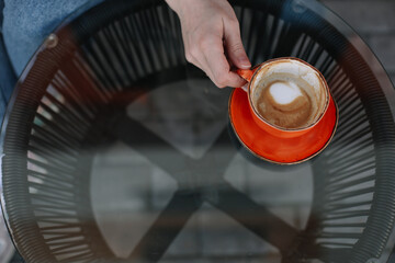 Woman's hands holding a big orange coffee cup top view