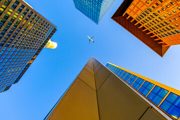 Buildings in the city with the sunny blue sky above and a plane on the sky. Airplane flies through...