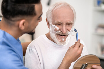 Caring volunteer giving a pleased old man a shave