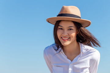 Portrait happy attractive young Asian woman wear hat looking at camera in the bright sunny day summer blue sky. Millennial lady with smiley face on her vacation holiday trip in tropical location