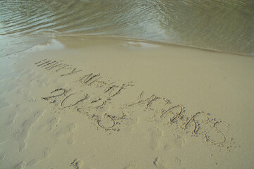 Happy New Year 2023 hand written on the sand in front of the sea.