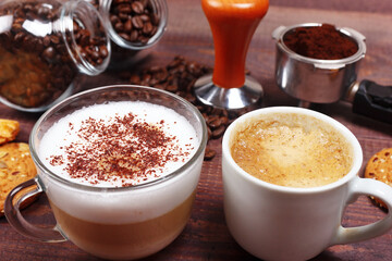Cups of espresso and cappuccino, crackers, holder with ground coffee, tamper and coffee beans on wooden table.