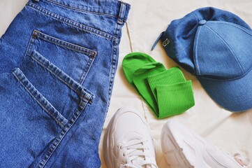 Flat lay photo blue jeans pants, denim cap, green socks and white sneakers. Sport chic style clothes top view fashion photography