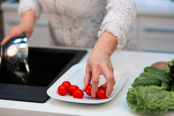 Hands of an elderly woman take cherry tomatoes from a plate, close-up