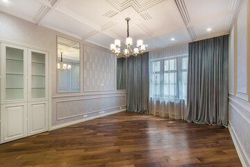 A spacious living room without furniture with original decorated walls and ceiling. Brown parquet.