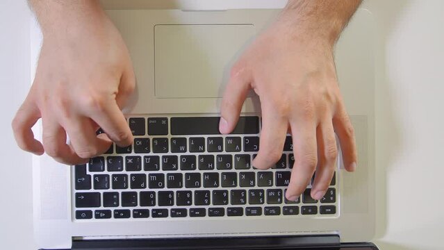 Young man typing on his silver laptop computer on the desk. Top view. 4K shot.