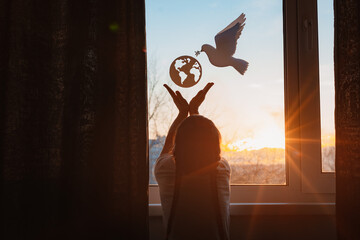 child stretches his hands sunlight outside window flying dove world with branch forces globe. concept peace world, no war, ecology