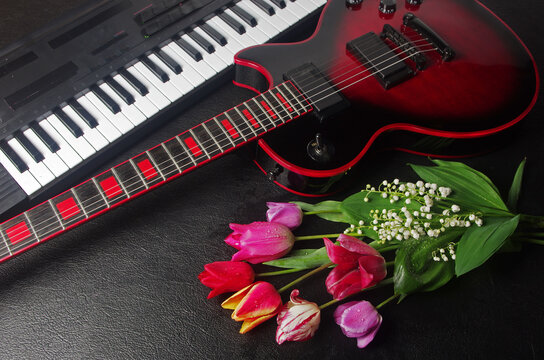Electric guitar, synthesizer keyboard, bouquet of tulips and lilies of the valley on a black table.