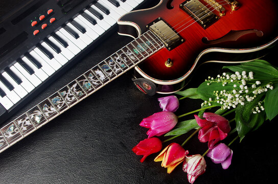 Electric guitar, synthesizer keyboard, bouquet of tulips and lilies of the valley on a black table.