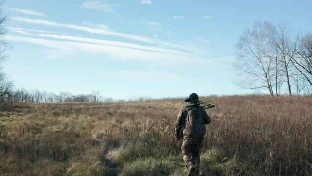Aerial, bowhunter in camouflage clothing walking alone on winter forest meadow