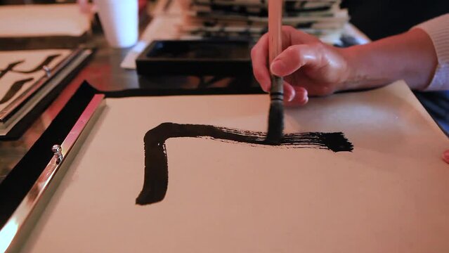 Close-up of a hand and a calligraphy brush. A person learns to hold a brush and draw elements of hieroglyphs on paper. A forbidden way to draw hieroglyph elements in calligraphy.