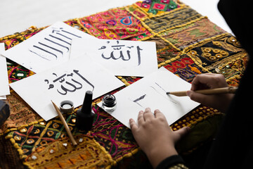close up muslim girl hands writing Arabic text with bamboo pens and black ink on paper, Arabic letters mean the name of Muslim god "Allah"