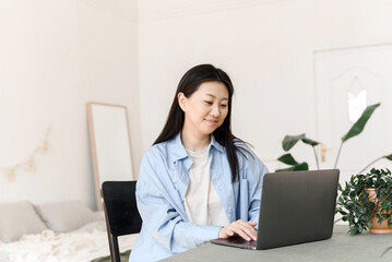 Portrait of young asian woman studying online or taking web course on computer at home, working on laptop from home office. The concept of distance education.