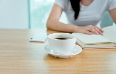 Woman reading book with cup of coffee on table