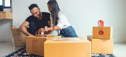 An Asian and Caucasian couple are packing boxes to move house, where they live happily using tape...