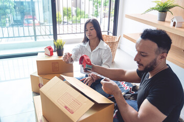 An Asian and Caucasian couple are packing boxes to move house, where they live happily using tape to seal the boxes in preparation for moving.