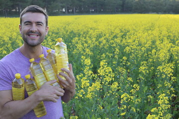 Farmer holding colza oil bottles with yellow flowers in the background