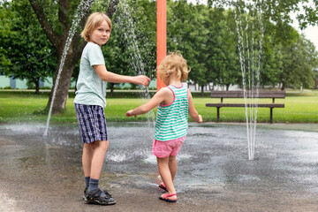 Small children playing at water splash pad fountain at park playground on hot sunny summer day. Happy kids having fun outdoors in summertime.