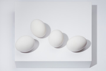 Still life of four white whole eggs on a white shelf and white background. Shallow depth of field