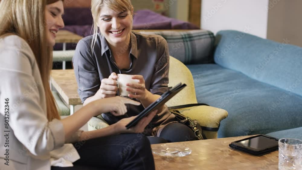 Poster cheerful businesswomen talking and laughing in a cafe while drinking coffee and using a wireless tab