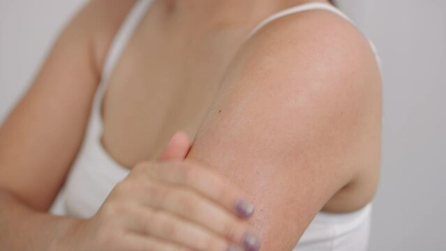 Woman rubs lotion body butter moisturizer on tricep upper arm wearing white tank top slow motion