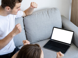 Online translation. Computer mockup. Winner excitement. Happy man and woman expressing euphoric joy looking laptop with blank screen in light room interior.
